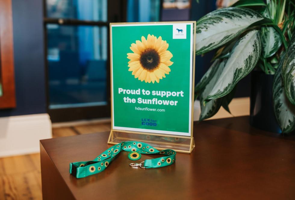 Green "Proud to Support the Sunflower" sign on a table with a sunflower lanyard laying next to it