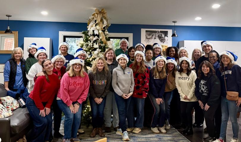 A group of adults posing in front of a Christmas Tree at the Ronald McDonald House.