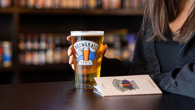 A Brewgrass Trail pint glass and guidebook sit on a table with a patron.