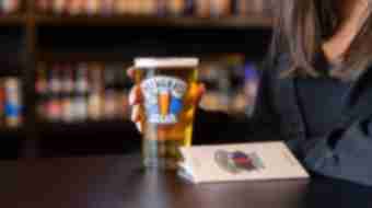 A Brewgrass Trail pint glass and guidebook sit on a table with a patron.
