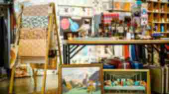 An array of antique bottles sits on a table with vintage suitcases below it and old framed paintings.